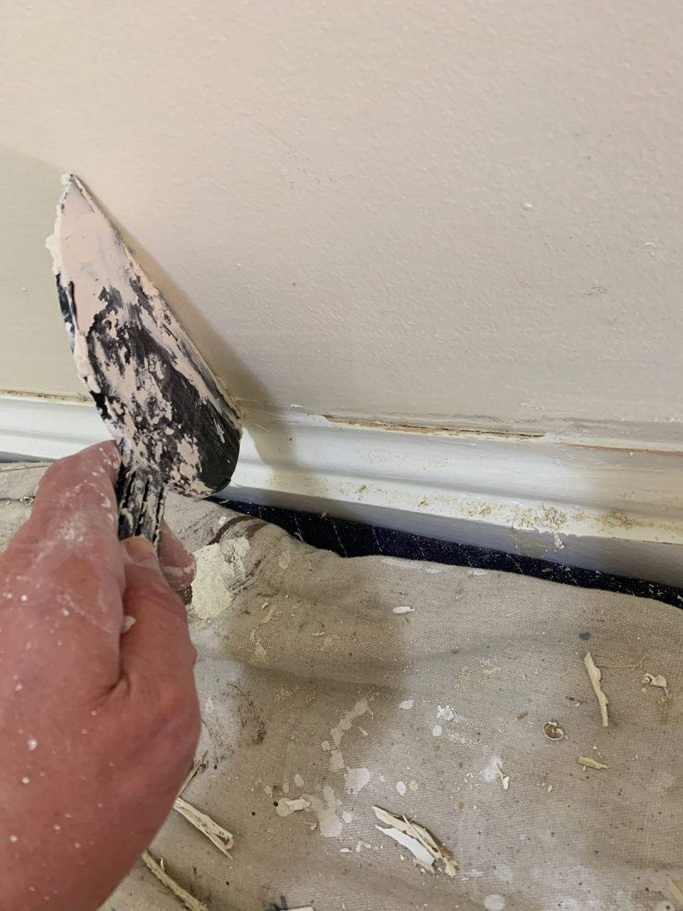 Applying putty to rebuild the damaged trim profile and patch the adjacent sheetrock surface before sanding.
